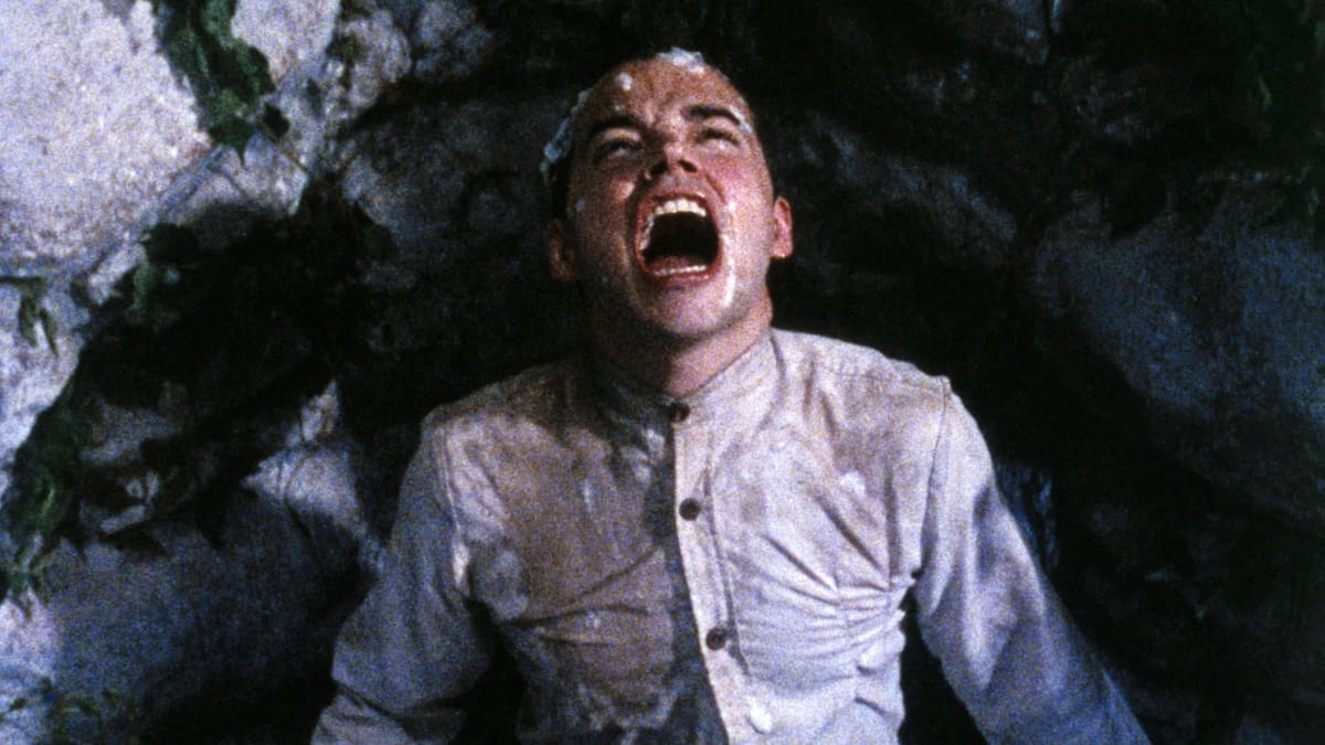 A young man looking toward the sky, mouth open and pained, drenched in the spit of other boys.